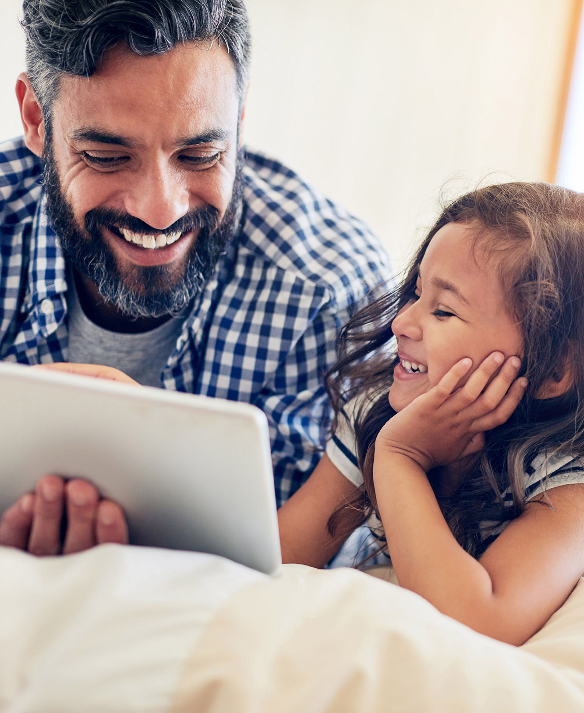 Father and daughter laying on a bed together looking at an ipad