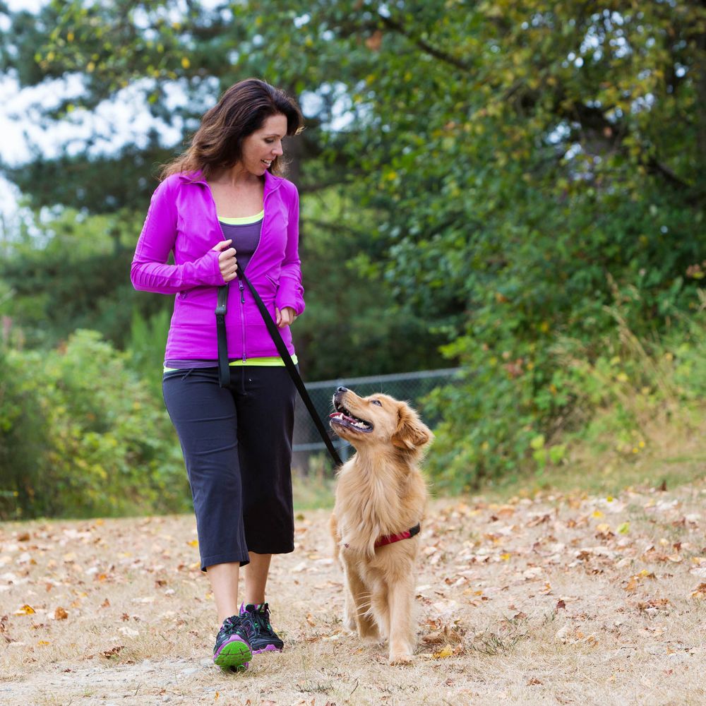 A woman wearing a pink jacket walking her dog on a trail.