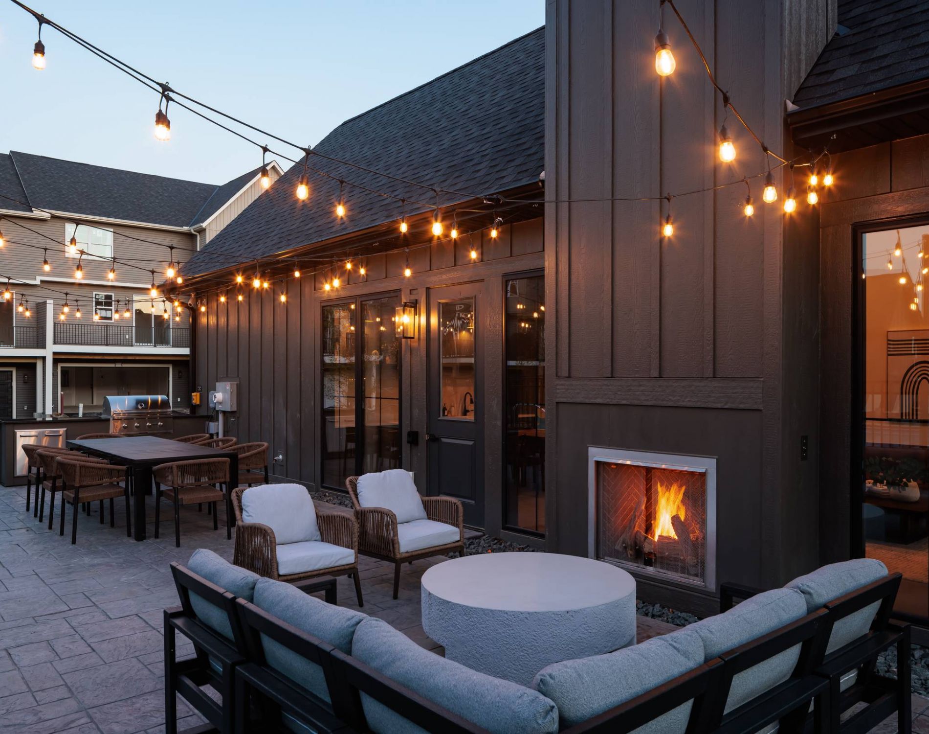 A cozy outdoor seating area at Olive Lane Townhomes with string lights and a firepit, providing a warm and inviting atmosphere at dusk.